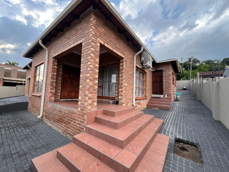 A well-maintained face brick house featuring a covered entrance porch, tiled steps, and a paved driveway with perimeter security fencing.