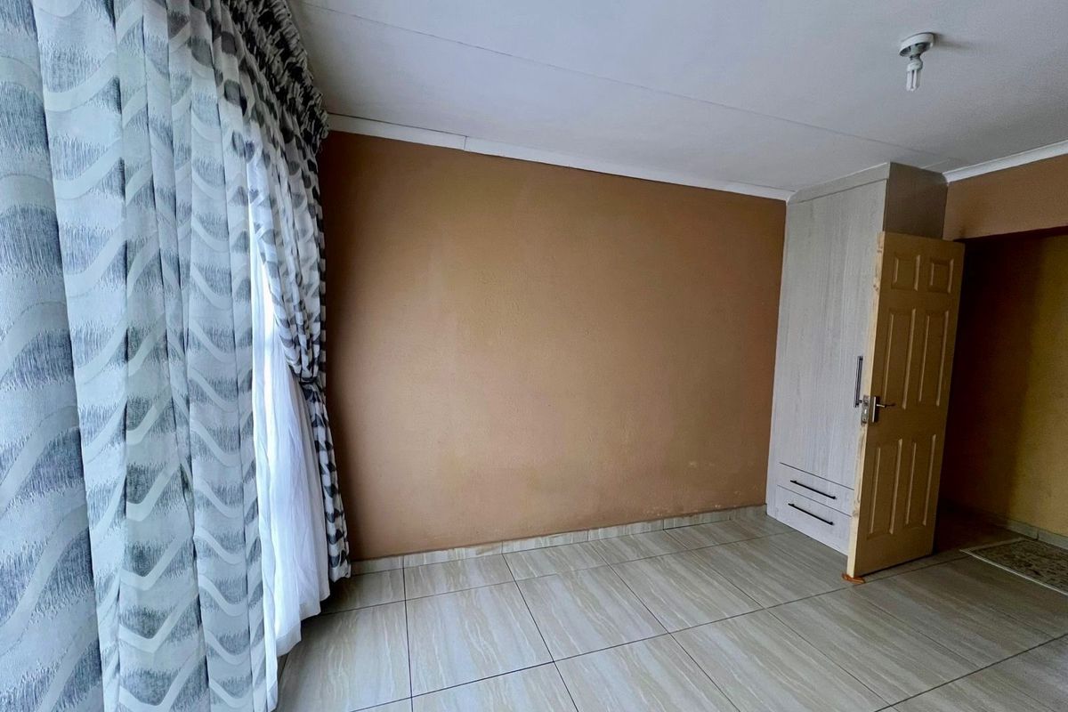 A vacant bedroom featuring tiled flooring, a built-in wardrobe, and a neutral wall finish, offering a blank canvas for personalization.
