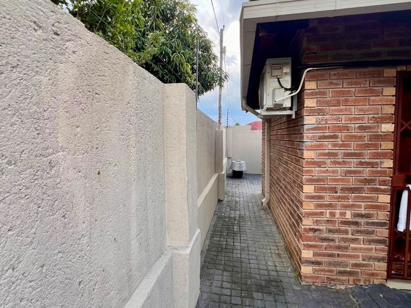 A narrow side passage featuring a paved walkway, brick exterior wall, and a mounted air conditioning unit.