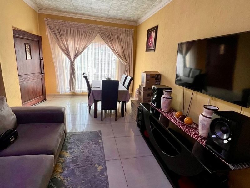Open-plan living and dining area featuring tiled flooring, textured ceiling tiles, and a timber entrance door.
