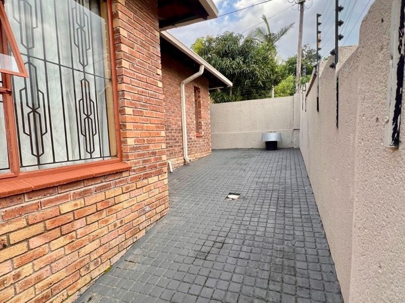 A side exterior walkway featuring brick wall construction, paved flooring, and perimeter security fencing.