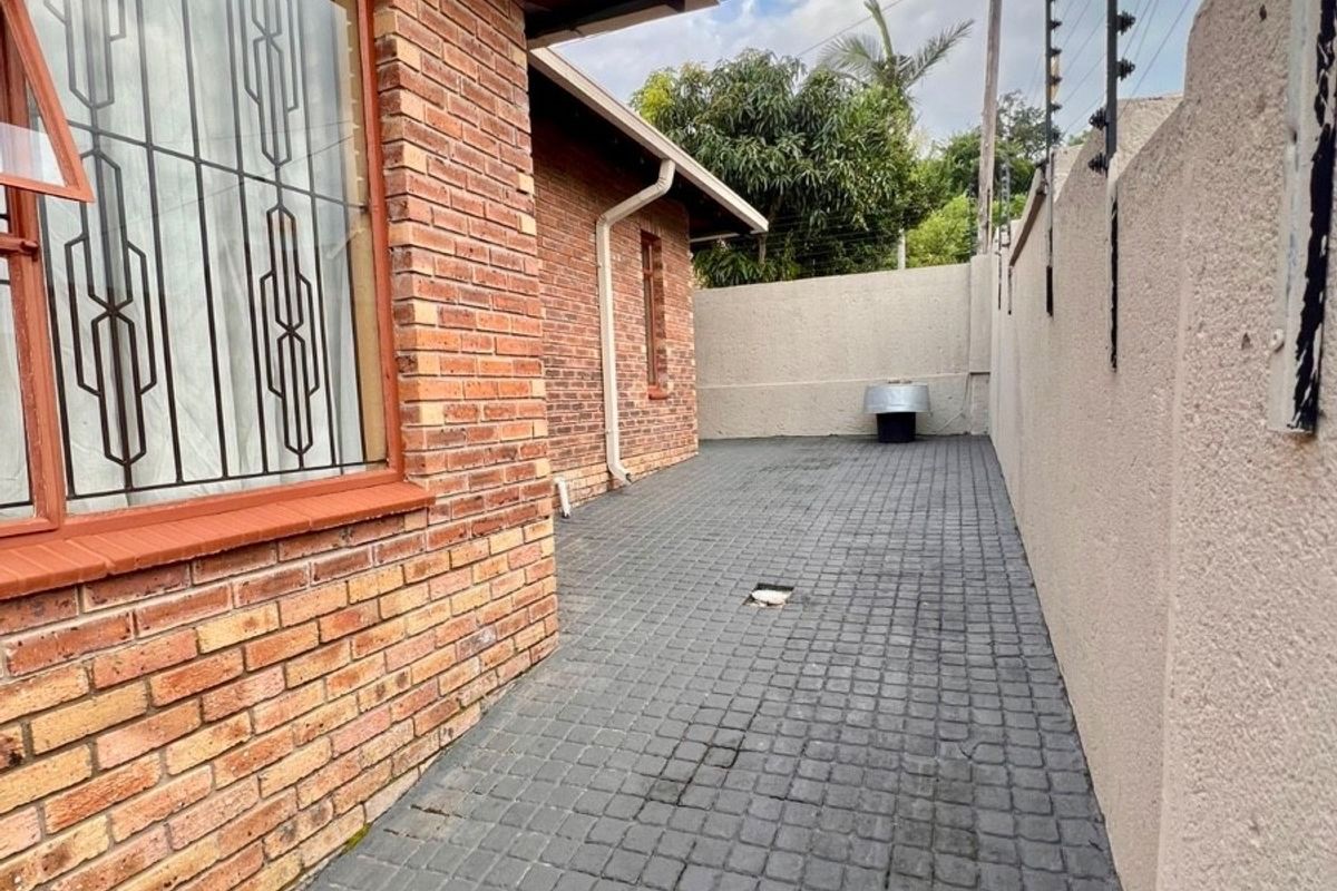 A side exterior walkway featuring brick wall construction, paved flooring, and perimeter security fencing.