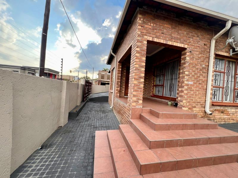 Front exterior view of a face brick house featuring tiled entrance steps, a paved driveway, and secure perimeter walling with electric fencing.