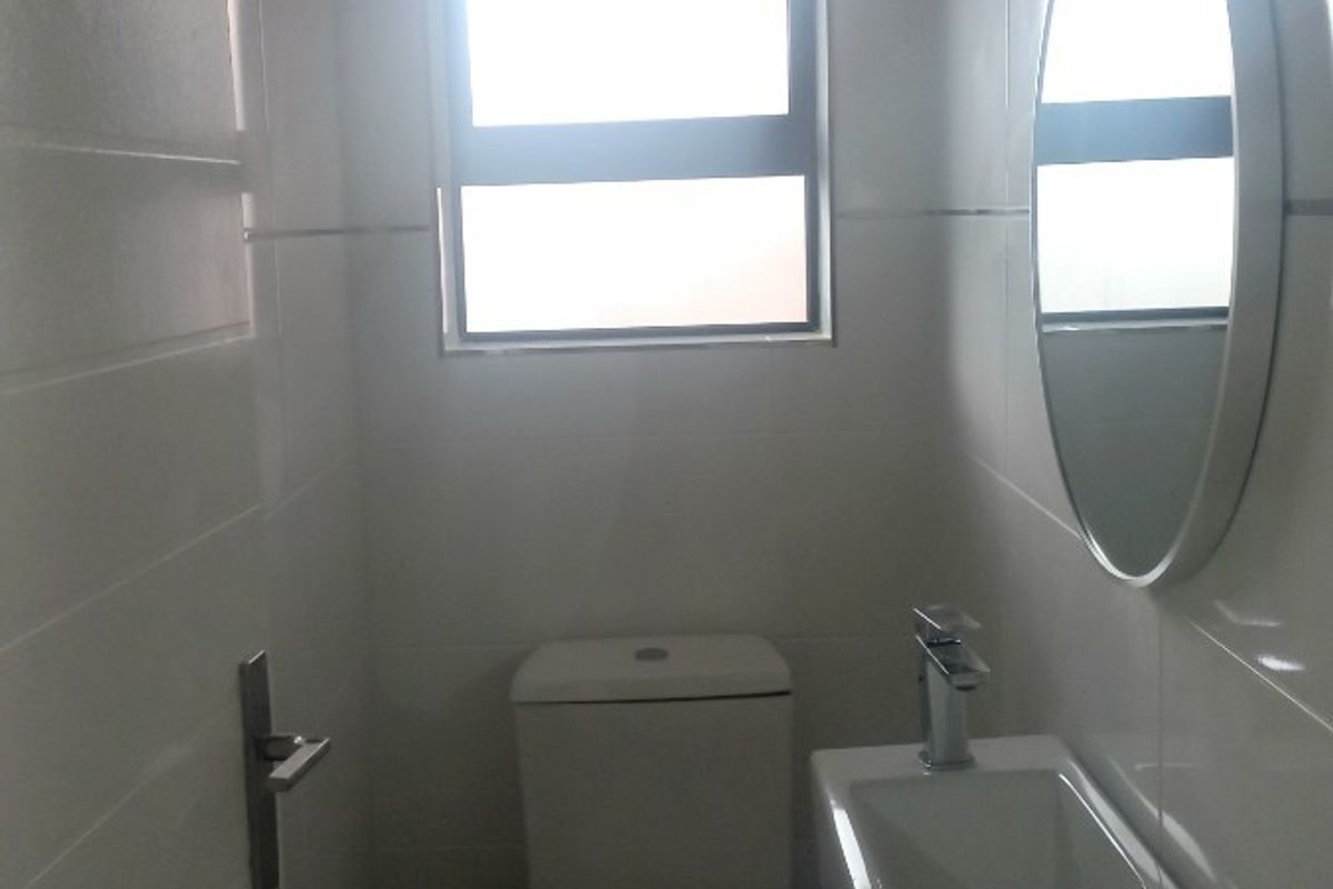 A compact guest bathroom featuring a wall-mounted basin, modern mixer tap, and a toilet, finished with clean white wall tiles.