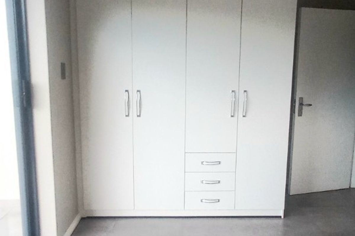 A bright, empty bedroom featuring modern grey tiled flooring and floor-to-ceiling built-in cupboards with a sliding door leading to an outdoor area.