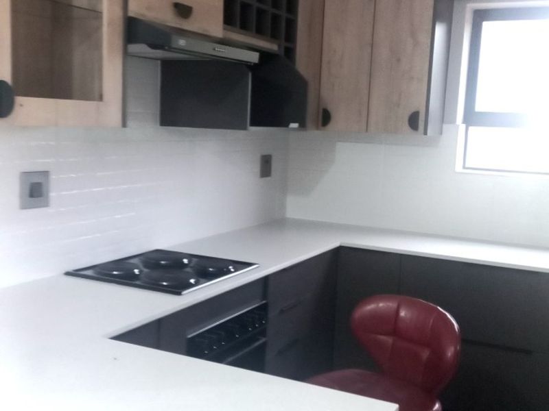 Modern kitchen featuring two-tone cabinetry, stone countertops, integrated electric hob, oven, and extractor fan with a clean tiled backsplash.