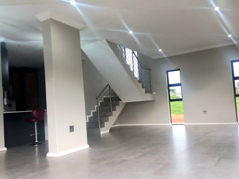 Spacious open-plan living area featuring modern tiled floors, a central staircase with stainless steel balustrades, and a sleek kitchen with built-in cabinetry.