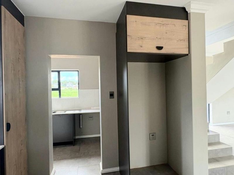 A modern kitchen area featuring built-in cabinetry, a dedicated refrigerator alcove, and tiled flooring, with an adjacent view into a secondary prep space.