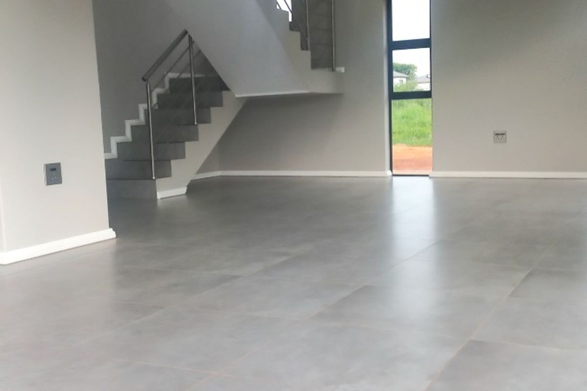 Spacious open-plan living area featuring modern large-format floor tiles, a contemporary staircase with stainless steel balustrades, and recessed downlighting.