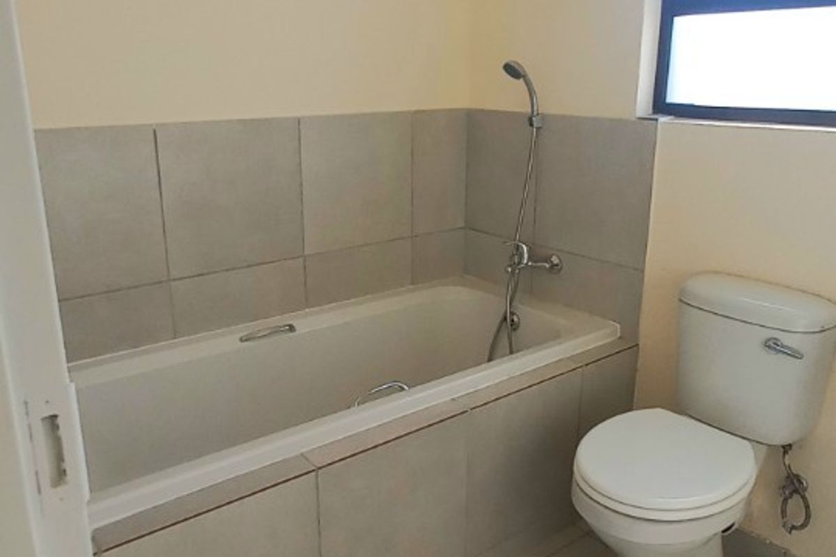 A functional bathroom featuring a tiled bathtub with shower attachment and a standard toilet, finished with neutral wall paint and floor tiles.