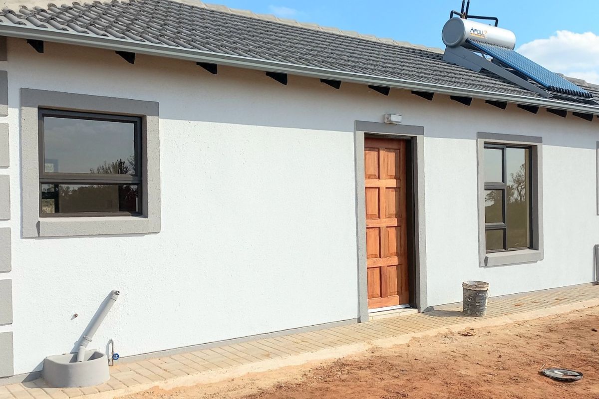 Exterior view of a modern single-story house featuring a tiled roof, solar water heater, timber entrance door, and paved walkway.