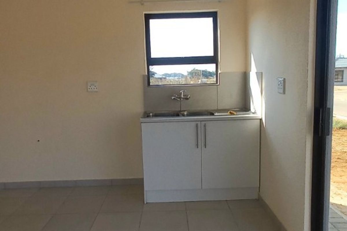 A compact kitchenette area featuring a single base cabinet, stainless steel sink, and tiled flooring, situated in an open-plan living space.