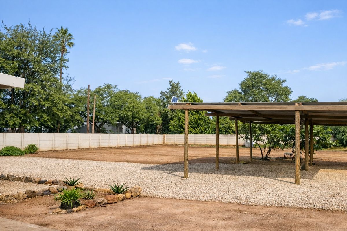 A spacious outdoor area featuring a large gravel yard and a covered timber carport structure, enclosed by a perimeter boundary wall.