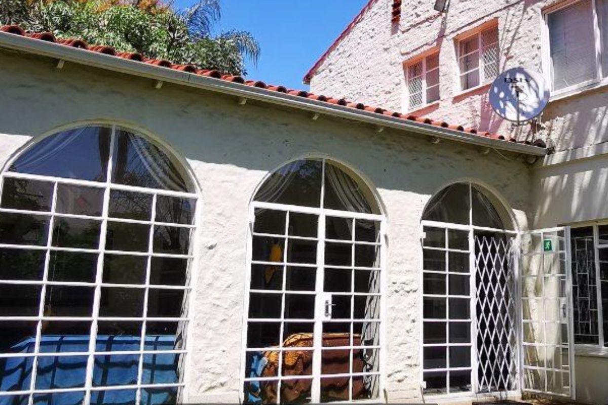 Rear exterior view of the house featuring arched glass doors, white textured masonry walls, and a terracotta tiled roof.