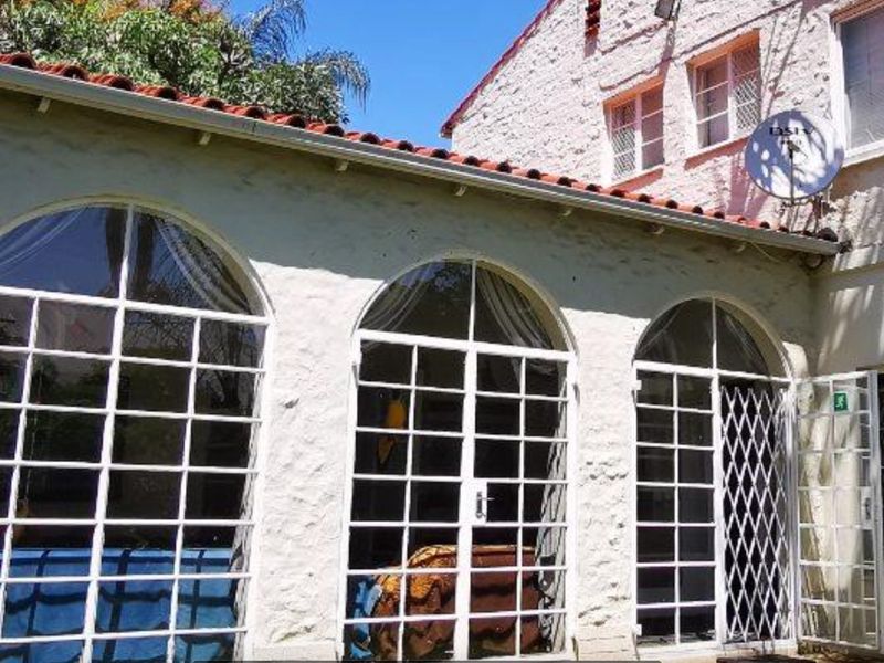 Rear exterior view of the house featuring arched glass doors, white textured masonry walls, and a terracotta tiled roof.