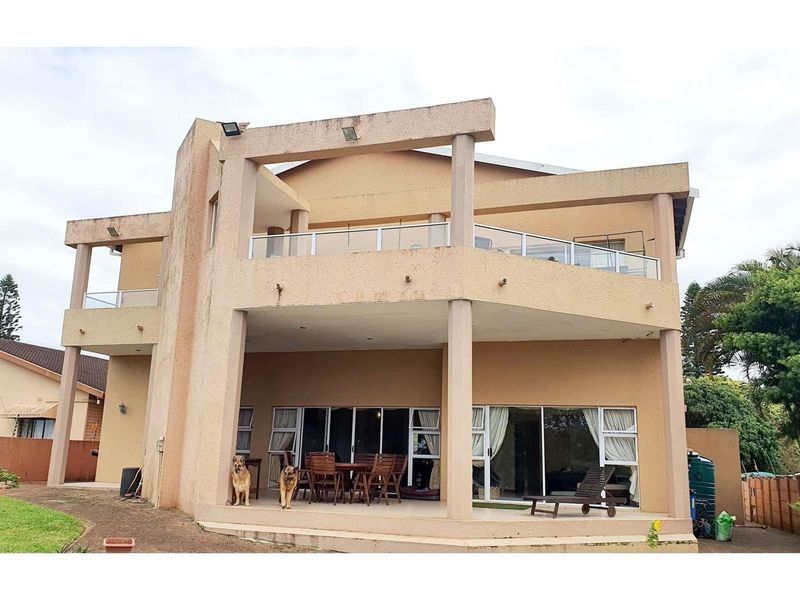 Rear elevation of a multi-story house featuring a covered patio, upper-level balcony with glass balustrades, and sliding door access to the interior.