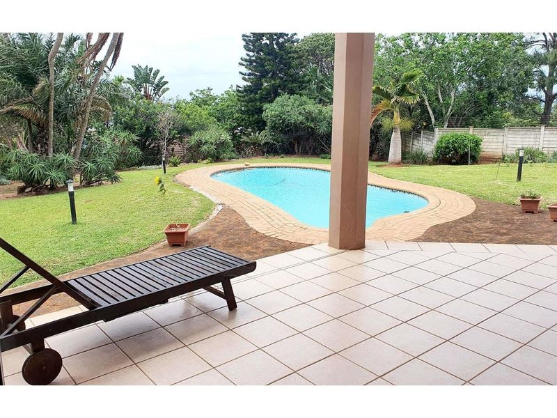 Covered tiled patio overlooking a landscaped garden and a swimming pool with brick coping.