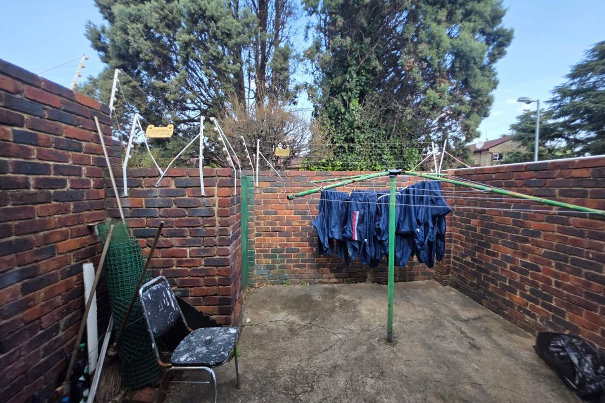 A private rear courtyard area featuring brick boundary walls, concrete paving, and a fixed rotary clothesline, offering potential for outdoor improvement.