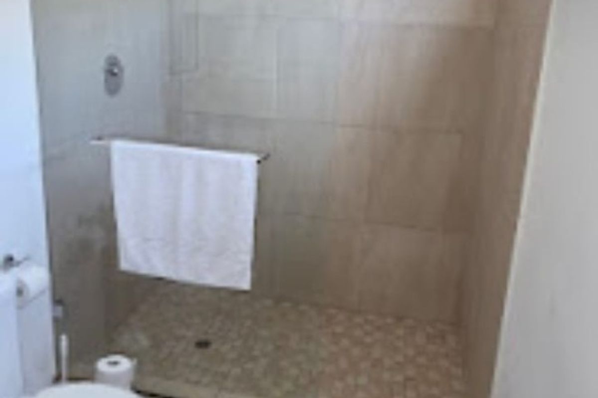 A functional bathroom featuring a walk-in shower with a glass screen, neutral wall tiling, and a standard toilet.
