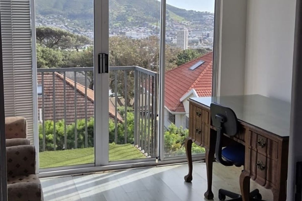 A bright bedroom featuring laminate flooring, recessed lighting, and a sliding glass door that opens onto a balcony with scenic mountain and city views.