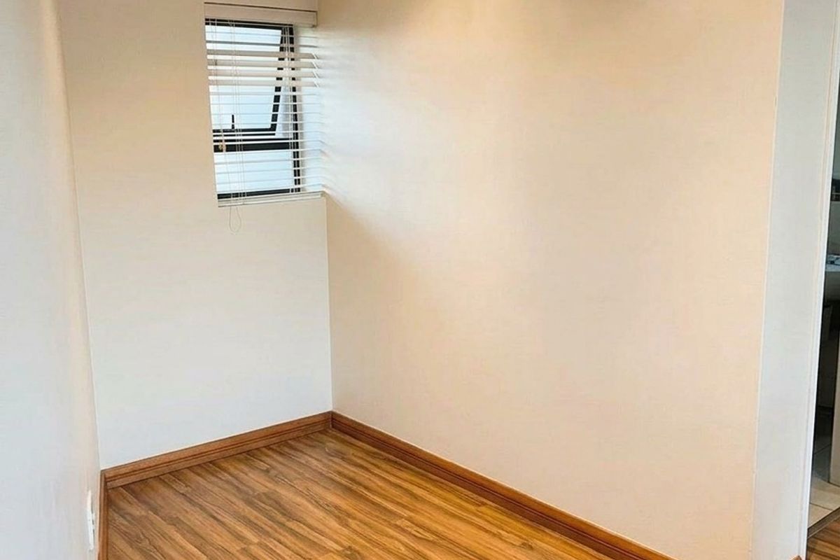 A bright, empty room featuring wood-look laminate flooring, neutral walls, and a small window with fitted blinds.