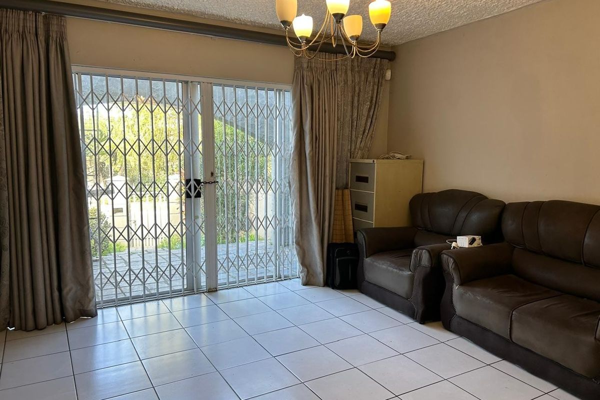 Living room featuring tiled flooring, a decorative chandelier, and sliding glass doors with security gates leading to an outdoor area.