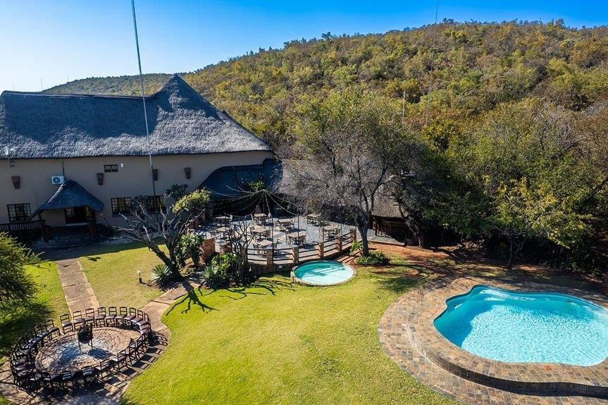 Aerial view of a farm property featuring a large thatched-roof building, a paved patio area, a swimming pool, and a landscaped garden.