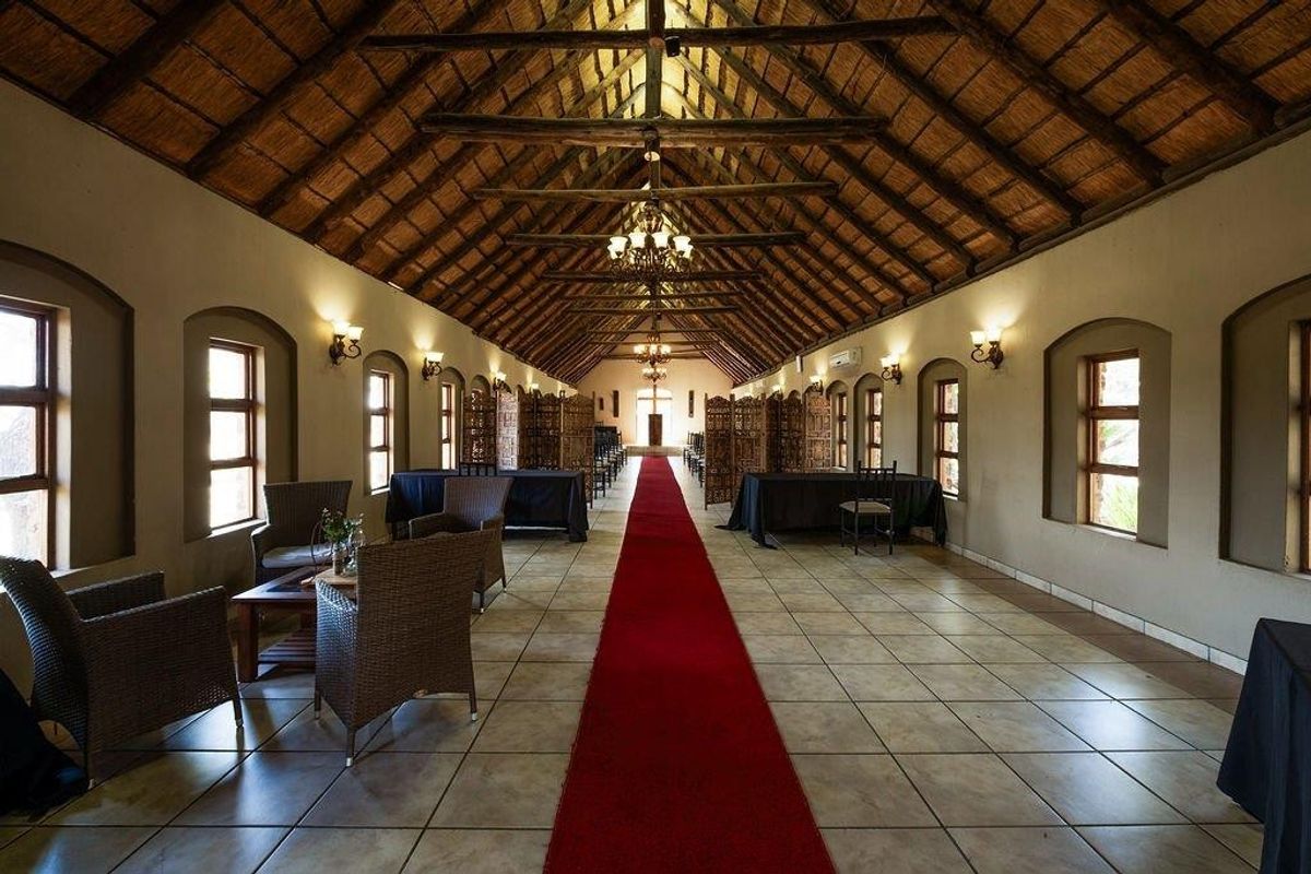Spacious event hall featuring a high vaulted thatched roof with exposed timber trusses, tiled flooring, and multiple arched windows providing natural light.