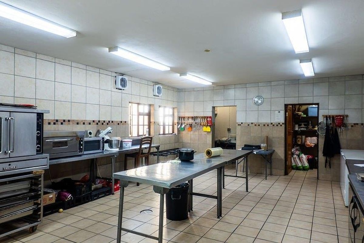 A functional commercial-style kitchen featuring stainless steel prep tables, industrial ovens, tiled walls, and fluorescent lighting, suitable for high-volume food preparation.