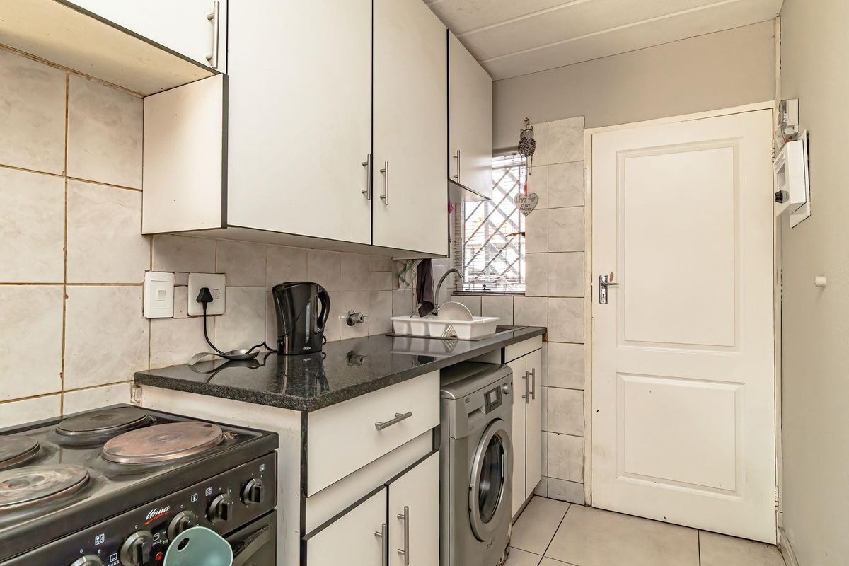 Compact kitchen featuring white cabinetry, dark stone countertops, tiled splashbacks, and integrated laundry plumbing, providing a functional workspace.