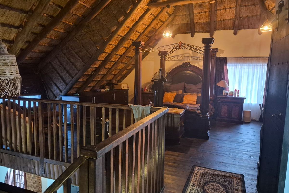 Spacious loft-style bedroom featuring a high vaulted thatched roof, exposed timber beams, and wooden flooring, creating a warm and rustic atmosphere.