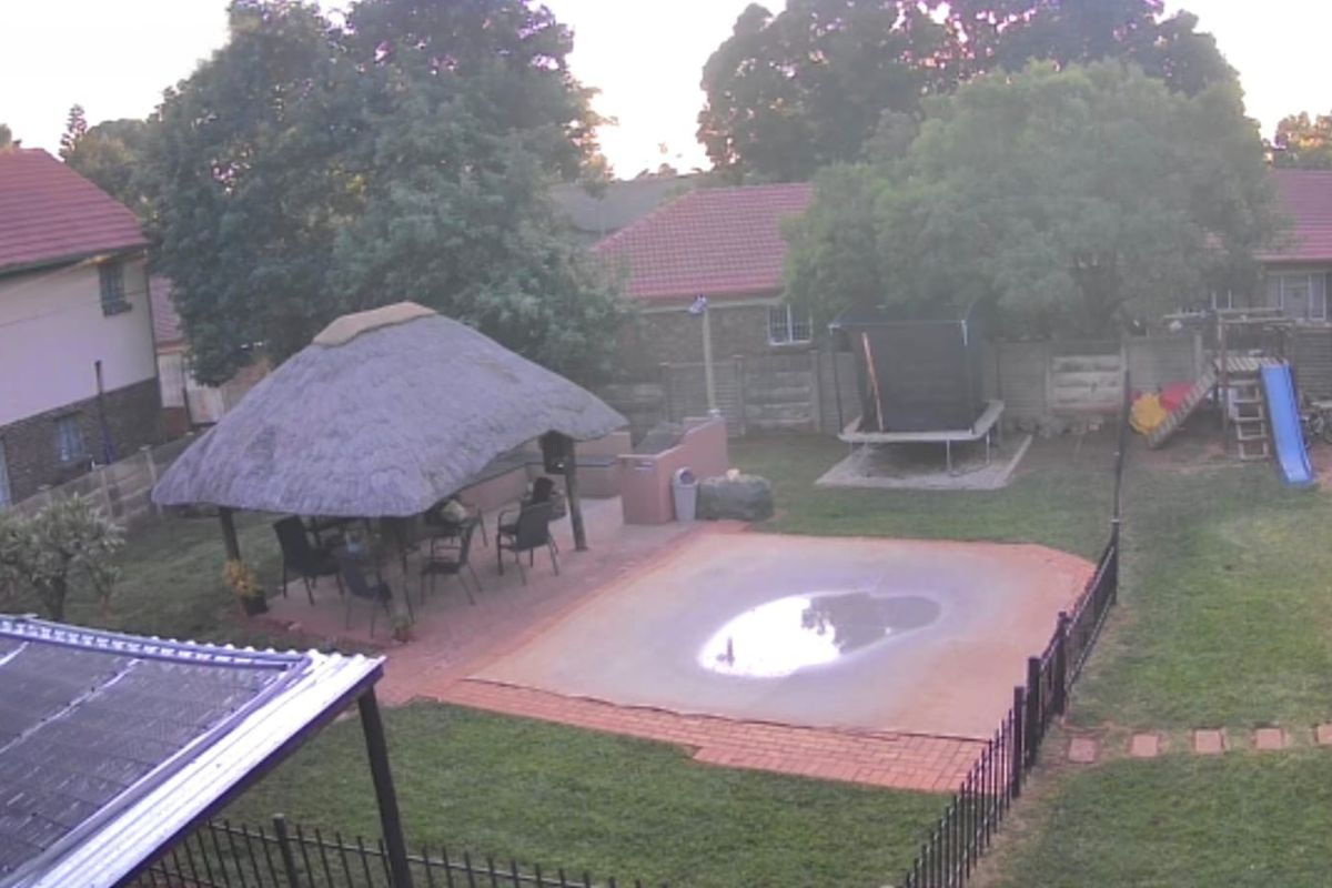 Spacious backyard featuring a thatched lapa entertainment area, a swimming pool with a cover, and a landscaped garden with perimeter walling.