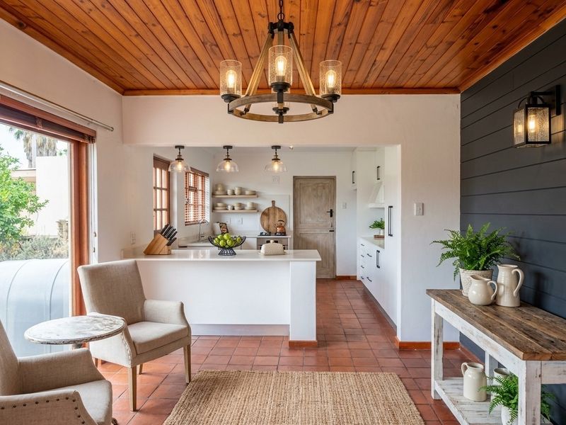 A bright open-plan living and kitchen area featuring warm timber ceilings, terracotta flooring, and a modern kitchen with stone countertops and stylish pendant lighting.