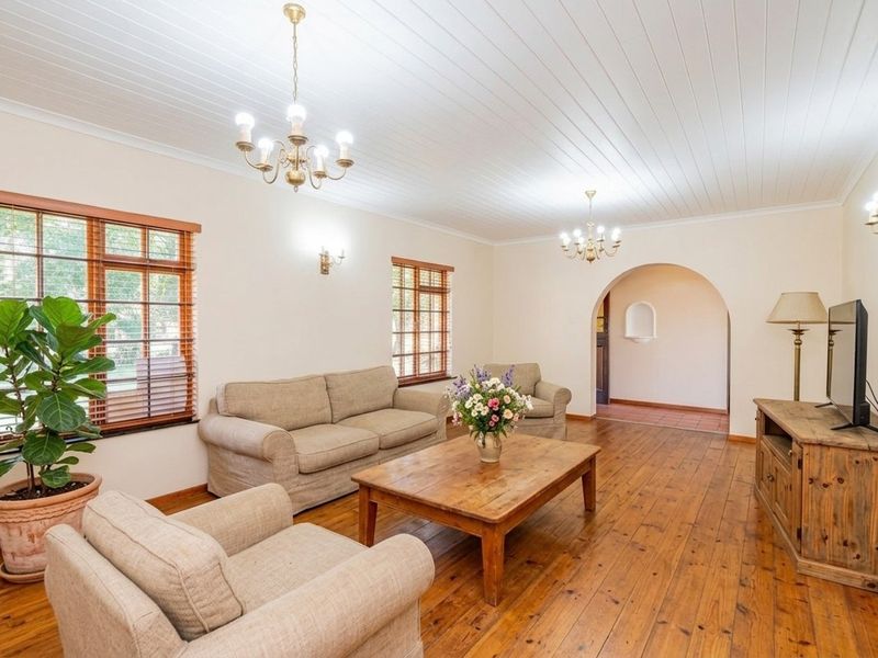 Spacious living room featuring warm timber flooring, a classic tongue and groove ceiling, elegant chandeliers, and a charming arched entryway.