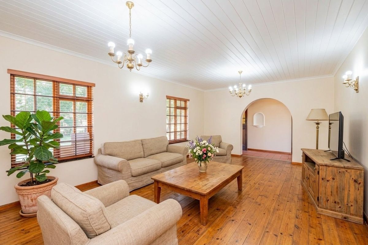 Spacious living room featuring warm timber flooring, a classic tongue and groove ceiling, elegant chandeliers, and a charming arched entryway.
