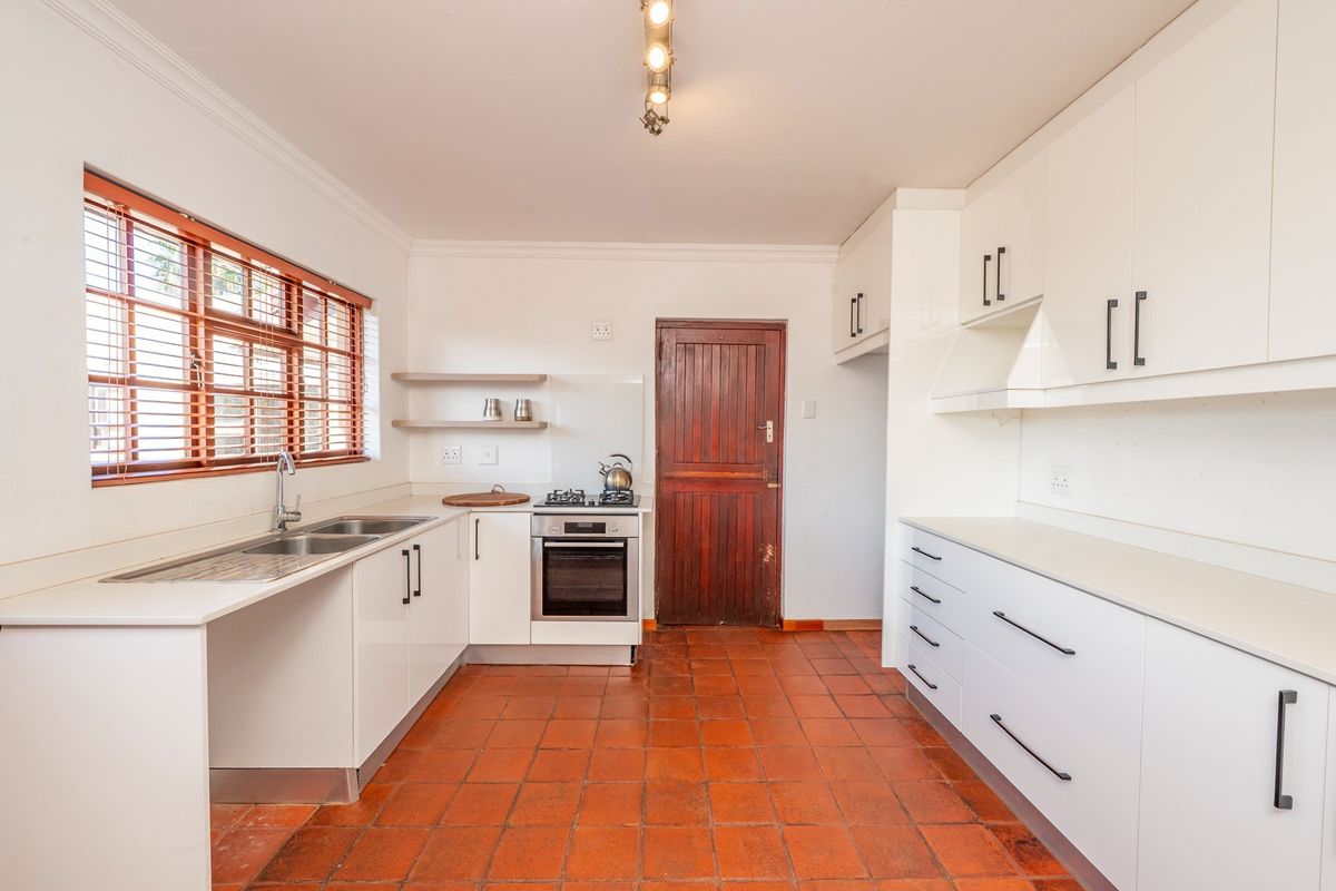 A functional kitchen featuring white cabinetry, built-in oven with gas hob, stainless steel sink, and traditional terracotta floor tiles.