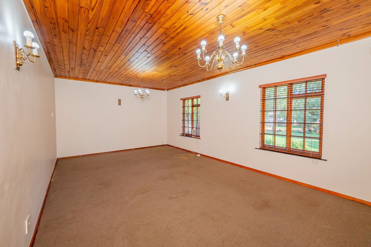 Spacious living area featuring a warm timber tongue and groove ceiling, classic brass chandeliers, wall sconces, and large windows with timber frames.