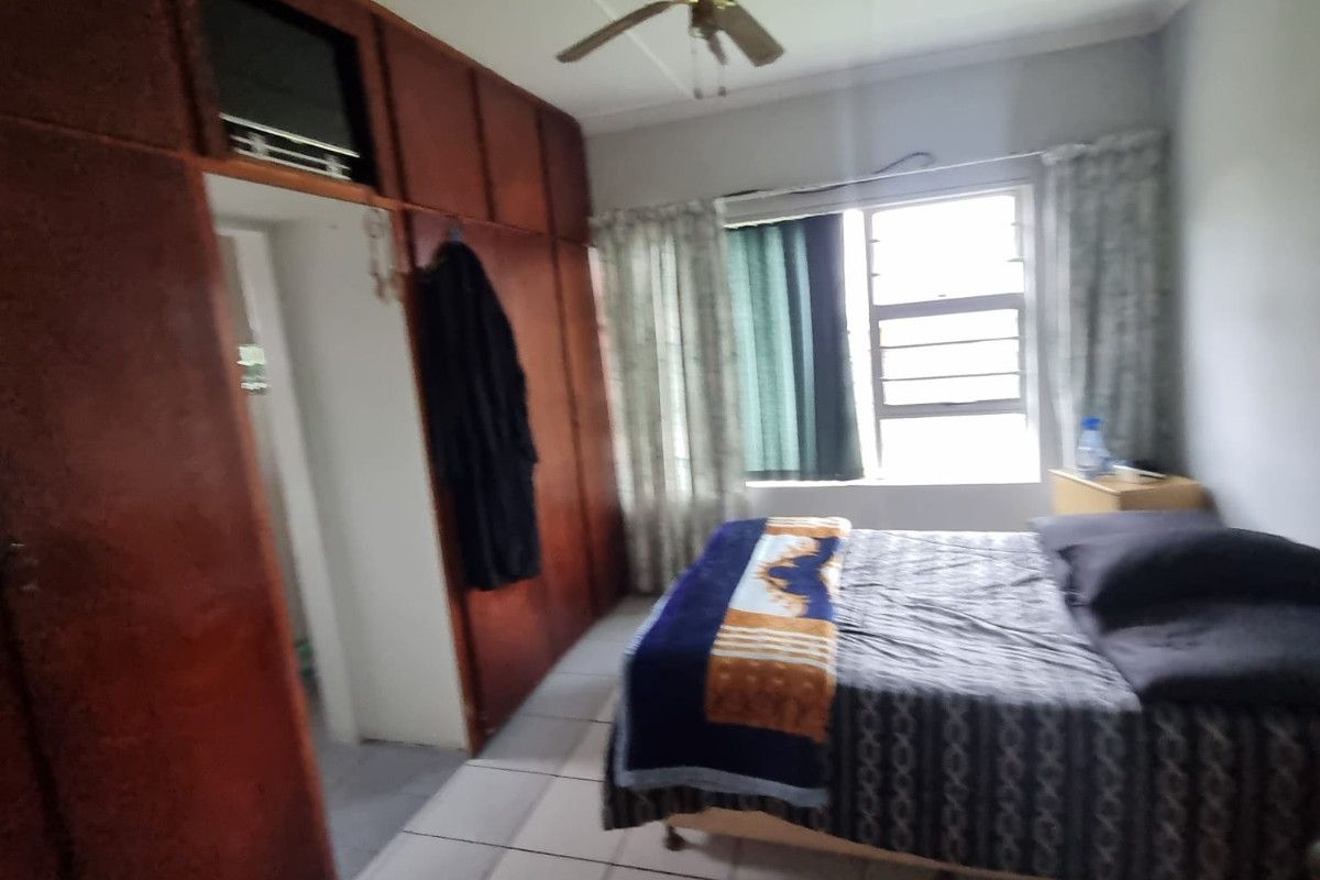 A bedroom featuring built-in wooden cupboards, tiled flooring, and a ceiling fan, offering a functional space with potential for cosmetic updates.