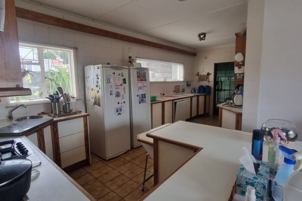A functional kitchen featuring dated cabinetry, laminate countertops, tiled flooring, and a ceiling fan, offering potential for a modern renovation.
