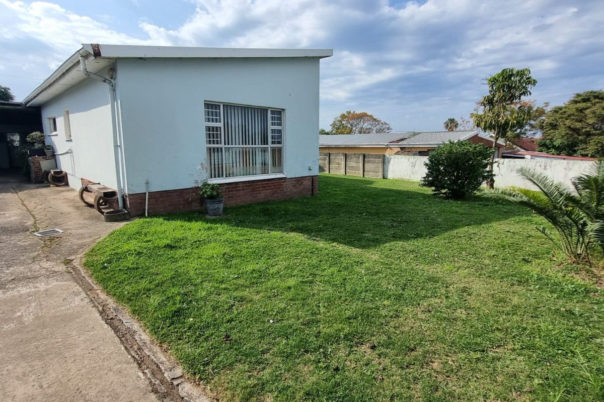 Rear view of the property featuring a lawn area, concrete driveway, and perimeter walling.