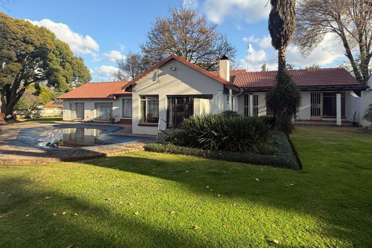 Rear view of the house featuring a swimming pool, landscaped garden, tiled roof, and paved patio area.