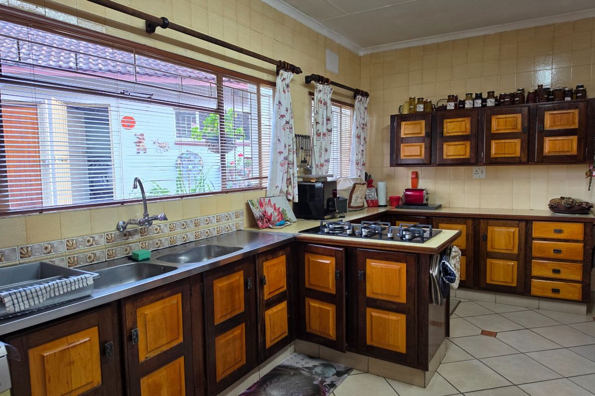 A functional kitchen featuring wooden cabinetry, a built-in gas hob, and a double stainless steel sink with tiled splashbacks.