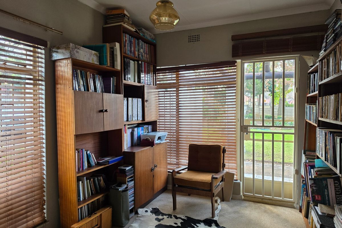 A sunlit study or bedroom featuring built-in shelving, carpeted flooring, and a security gate providing direct access to the garden.