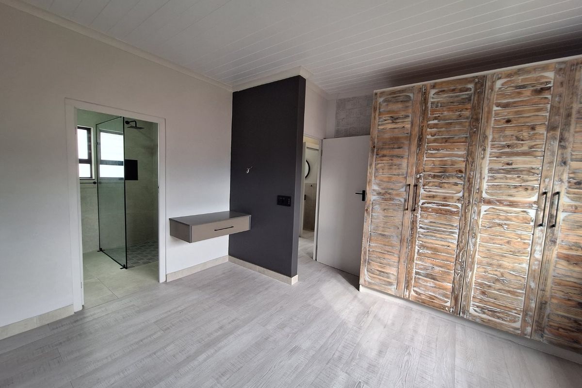 A bedroom featuring built-in wooden wardrobes, a floating vanity, and an en-suite bathroom with a glass-enclosed shower.