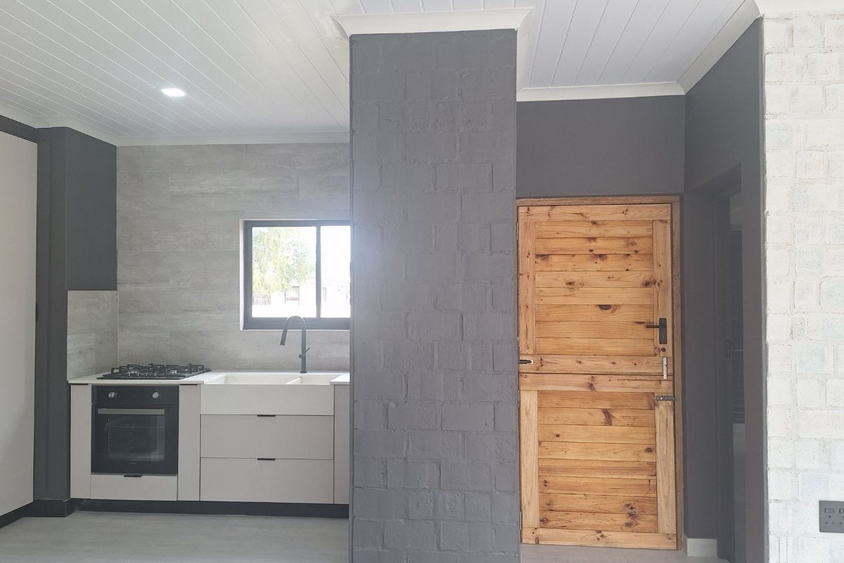 Modern kitchen area featuring built-in cabinetry, integrated oven and gas hob, stone-look splashback, and a distinctive rustic timber door.