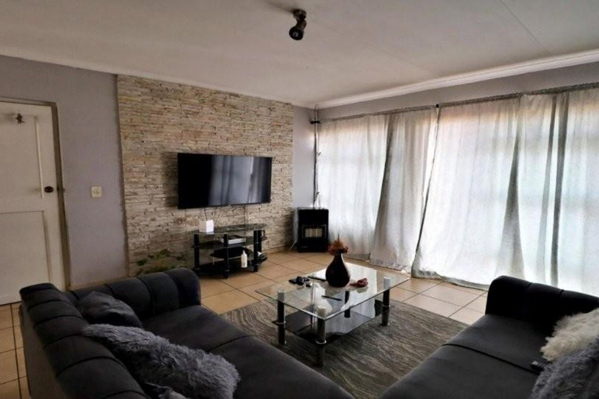 A living room featuring a textured stone feature wall, tiled flooring, and large windows with curtains, providing a bright and functional living space.