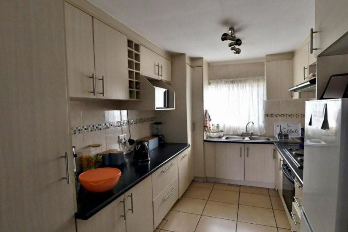 A functional galley-style kitchen featuring light wood-finish cabinetry, dark countertops, tiled flooring, and a double basin sink with a window view.