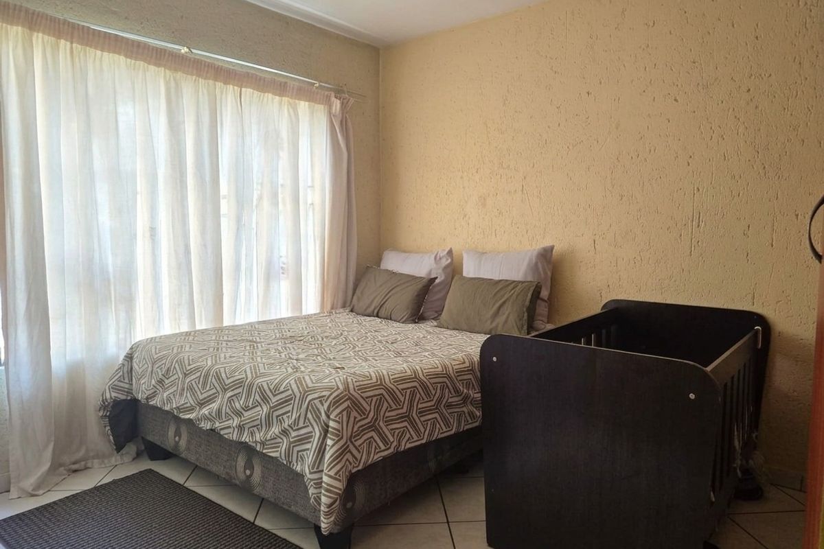 A bedroom featuring tiled flooring and a large window with curtaining, providing natural light to the space.