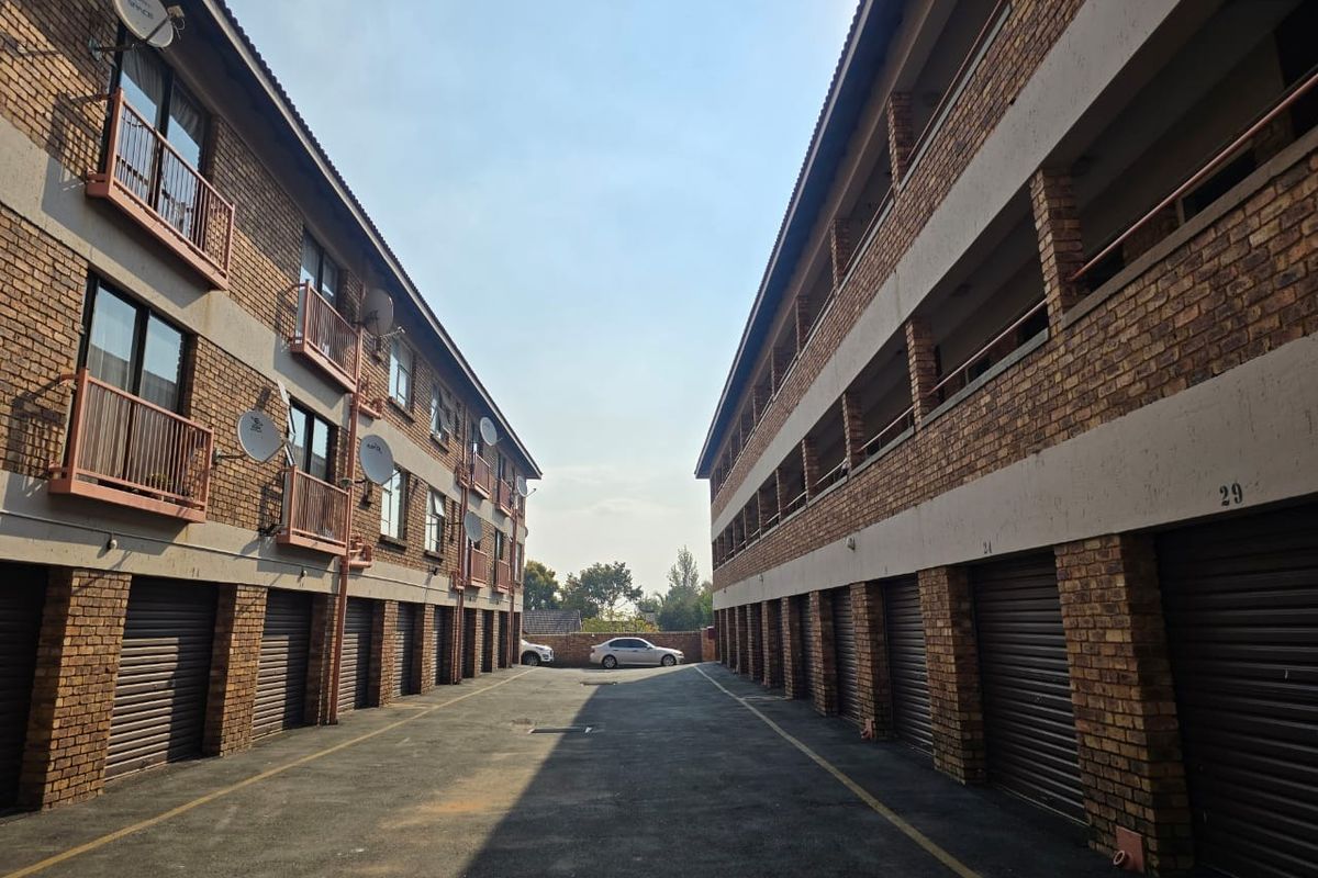 Exterior view of an apartment complex featuring a central driveway with ground-level garage units and upper-level balconies with brick facade construction.