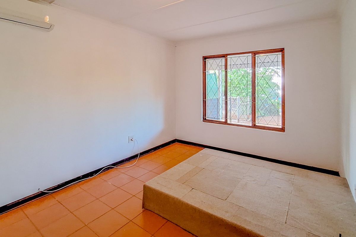 A bright, empty bedroom featuring tiled flooring, a built-in raised platform, and a wall-mounted air conditioning unit.